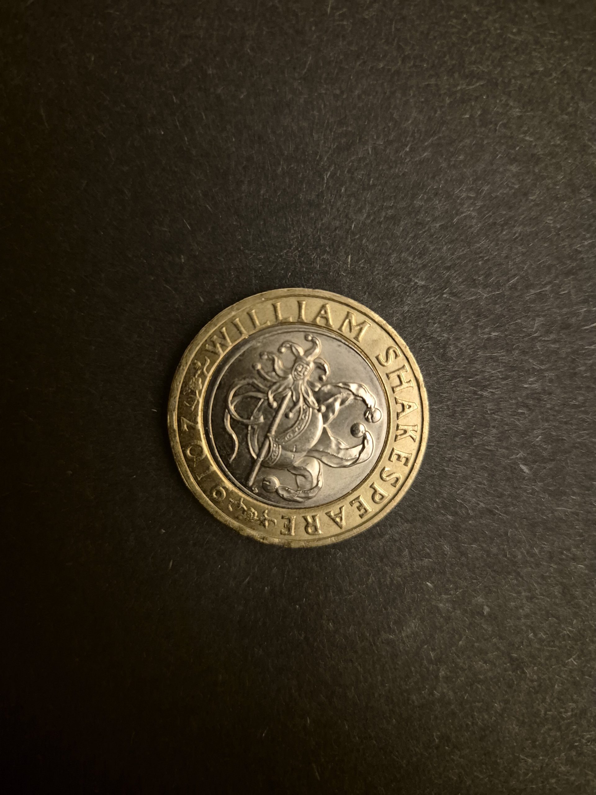 2016 William Shakespeare £2 Commemorative Coin - UK Currency Close-up of a 2016 British two-pound coin featuring a design commemorating William Shakespeare. The coin shows a depiction of a jester.